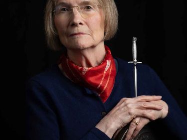 Author Danuta Reah, who has also written as Danuta Kot and Carla Banks, sits on a chair, holding a small dagger
